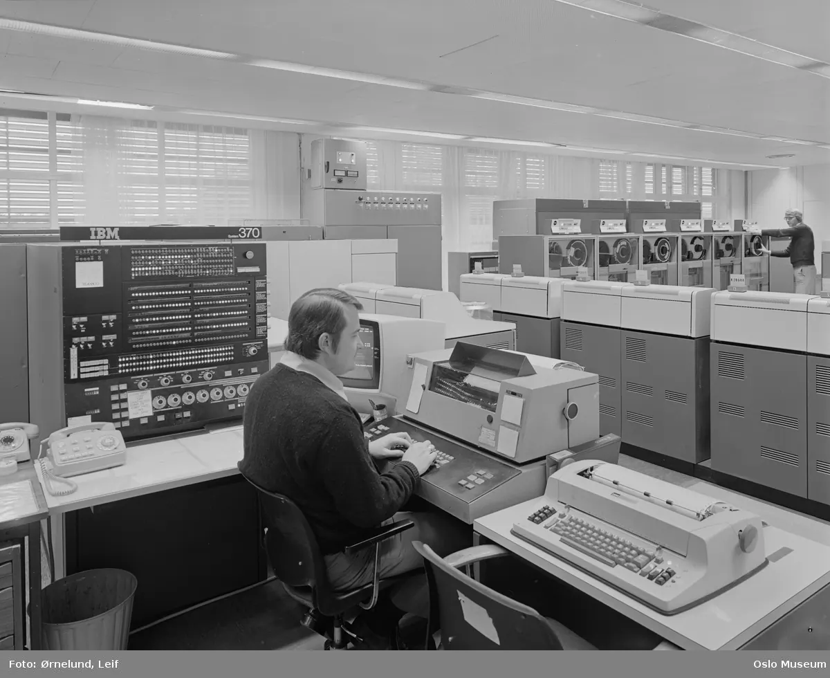 Phòng máy tính IBM System/370 thập niên 1970, nhân viên ngồi vận hành trước bàn điều khiển