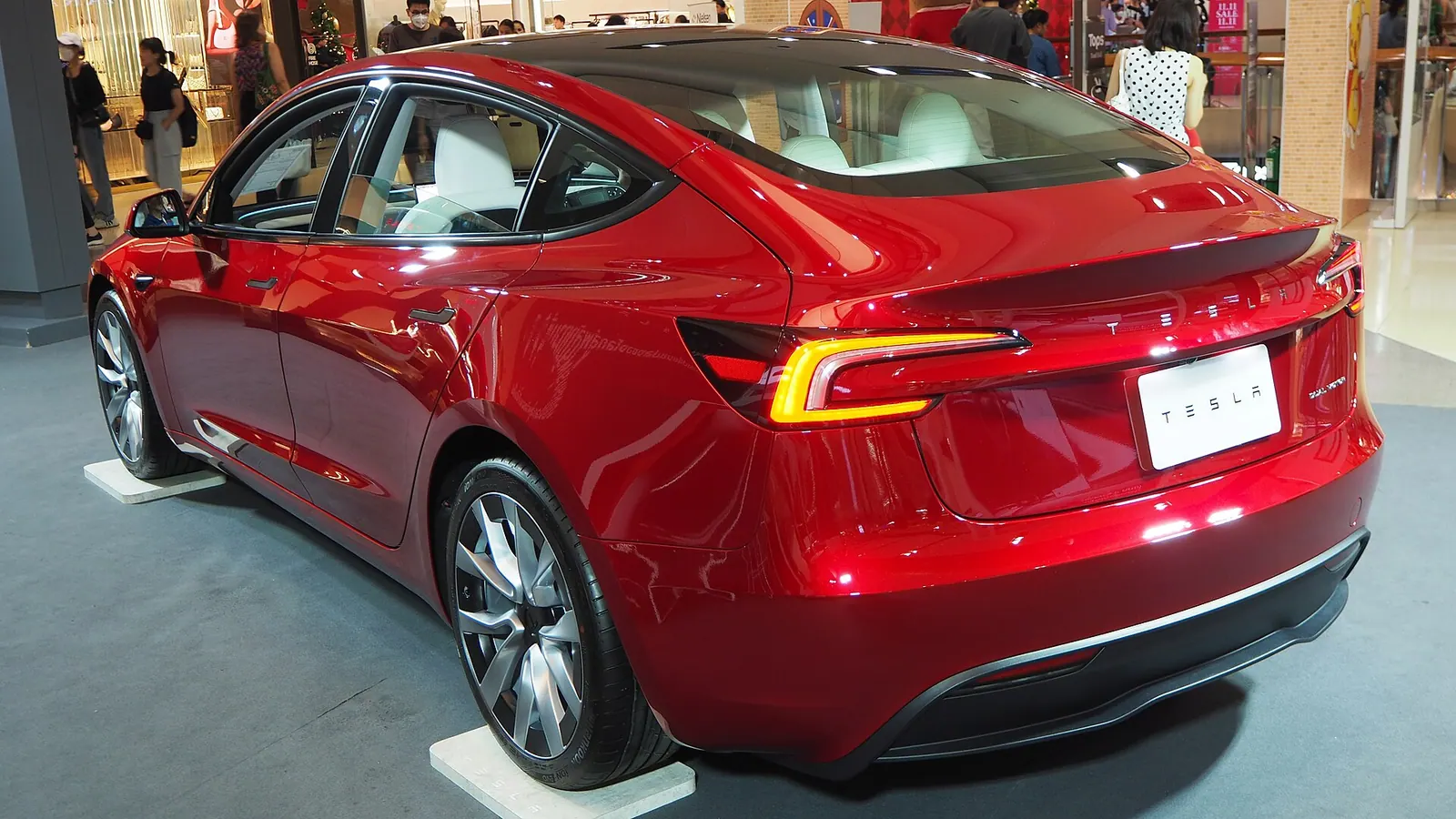Tesla Model 3 Highland màu đỏ trưng bày trong trung tâm thương mại, nhìn từ phía sau với logo Dual Motor