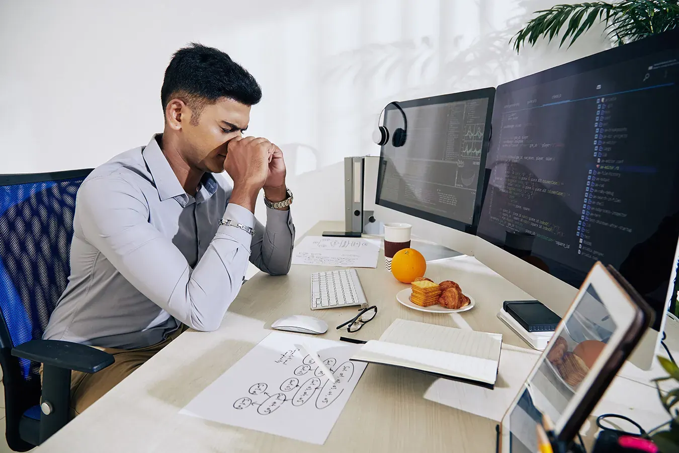 Lập trình viên ngồi trước nhiều màn hình mã nguồn, tay day sống mũi vì mệt mỏi
